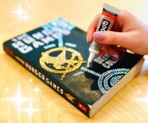 Image of a hand bedazzling the cover of the Hunger Games by Suzanne Collins.