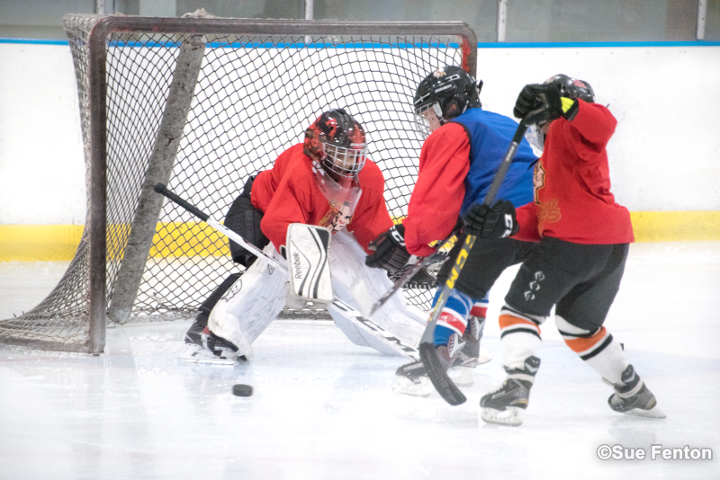 Youth hockey players trying to score while goalie defends goal
