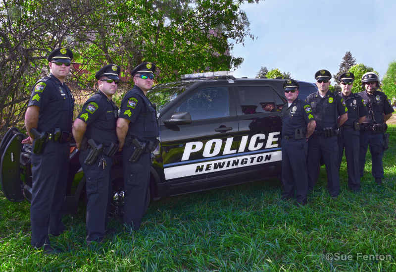 Seven members of the Newington Police Department posing for photo in front of fleet vehicle