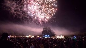 Firework bursting in the air with red, green and gold colors with hundreds of people gazing up at th