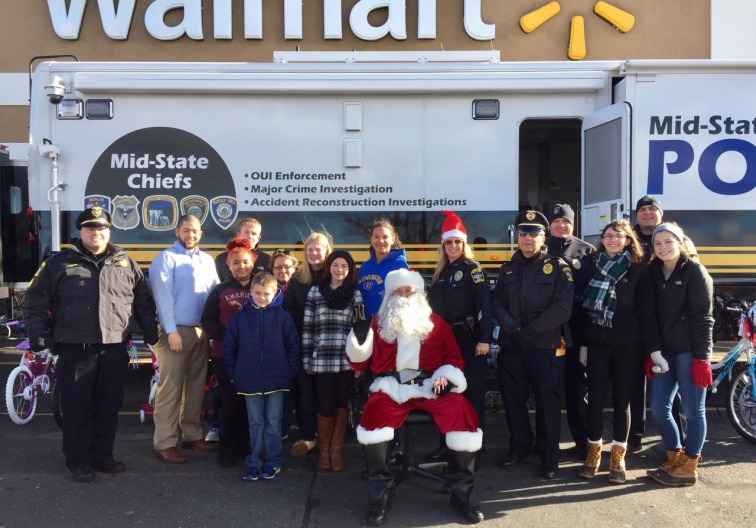 Multiple officers and volunteers with Santa at Walmart in front of command vehicle.