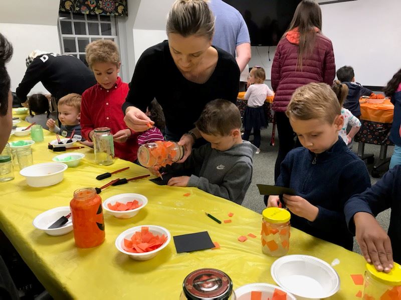 families making pumpkin luminaries with orange tissue paper and Mason jars